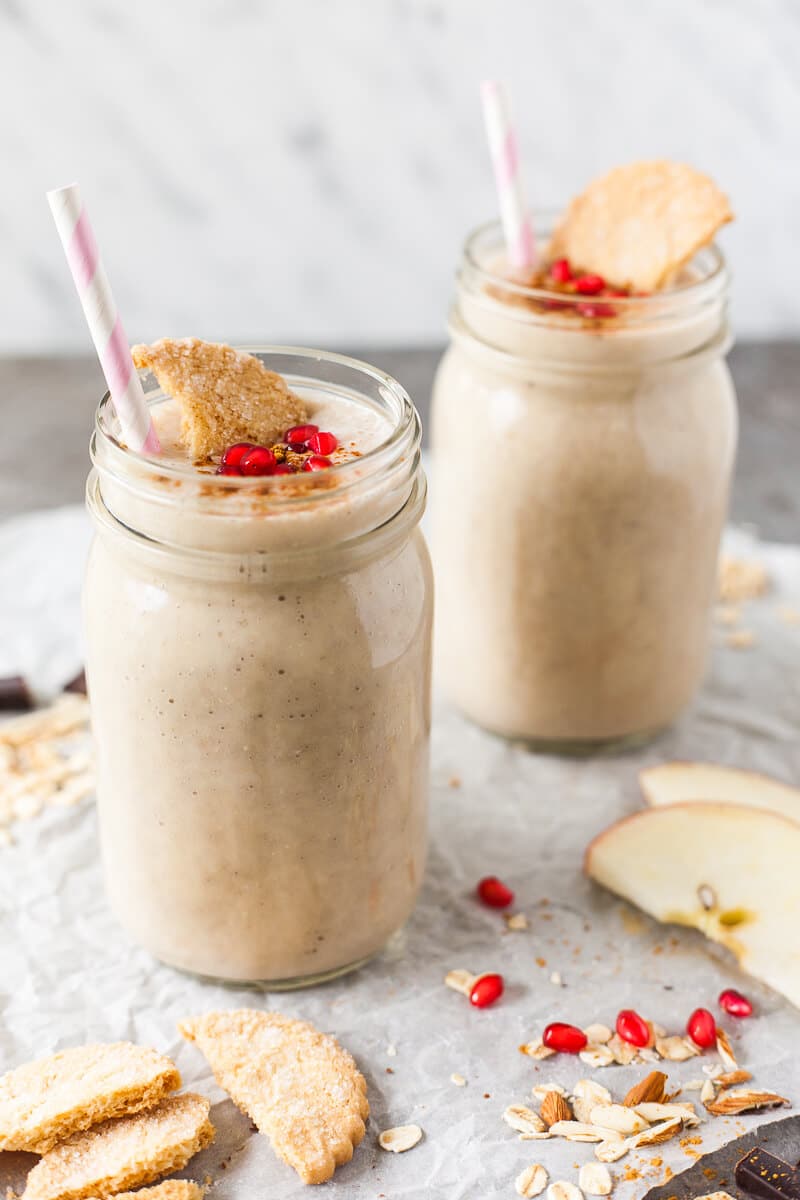 Two jars full of apple banana smoothie, topped with cookies and a few pomegranate seeds.