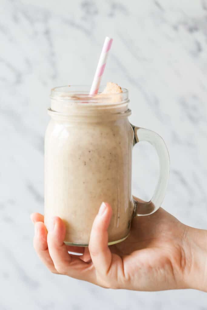 A hand is holding a jar of apple banana smoothie.