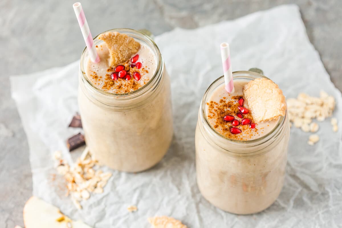 Two jars full of apple banana smoothie, topped with cookies and pomegranate seeds.