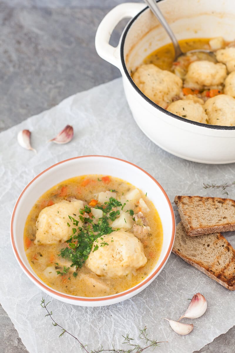 Chicken stew with fluffy dumplings is served in a bowl. A pot of stew is visible at the side.