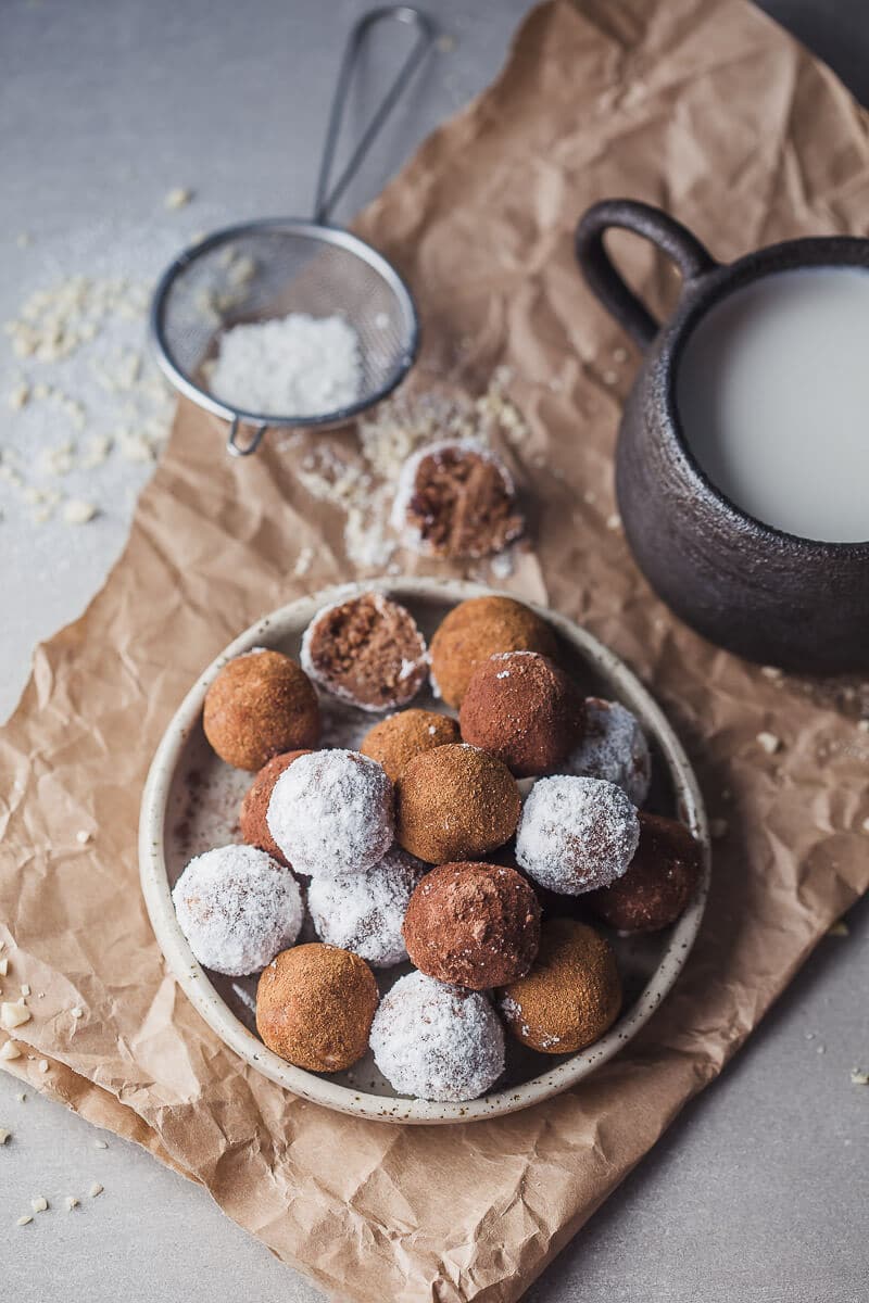 Almond pulp energy bites pictured from above. There's a cup of milk to the side. Somebody already took a bite in one of the energy bites.