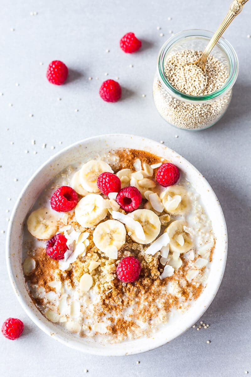 A top down picture of a quinoa bowl, topped with raspberries and banana. There's a small jar of uncooked quinoa in the top right corner.