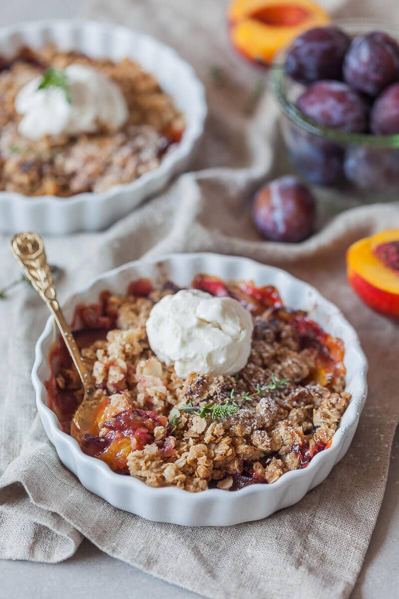 Plum crumble served in a bowl with a scoop of ice cream on top.